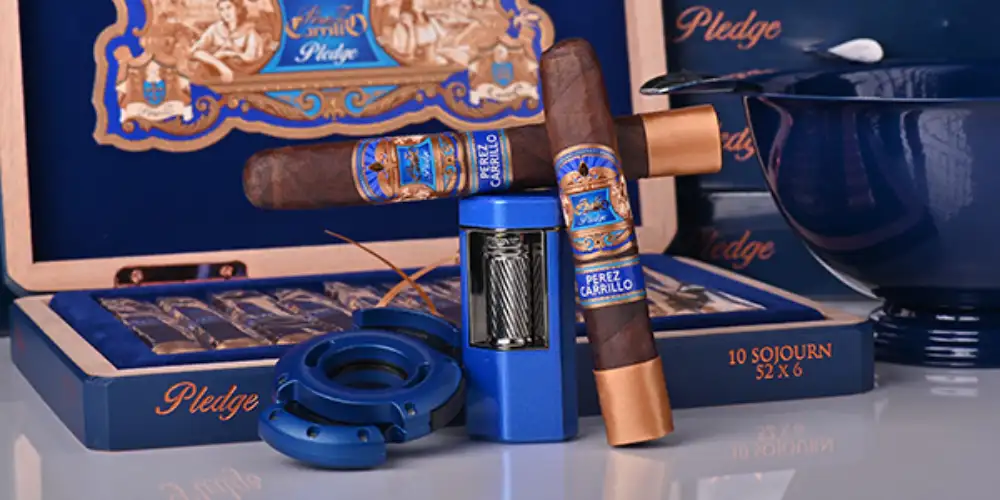 Zigarre der Marke E.P. Carillo Pledge neben der Kiste und Xikar Zigarren-Zubehör