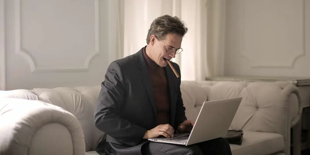 Mann mit Zigarre im Mund sitzt vor einem Laptop
